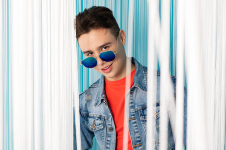 Portrait of a handsome young man in denim clothes posing against a bright, creative room decorated...