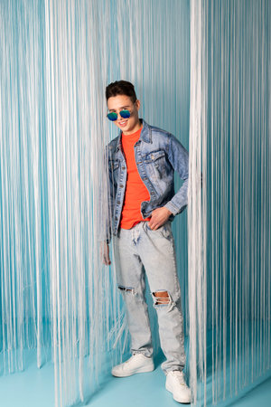 Portrait of a handsome young man in denim clothes posing against a bright, creative room decorated...