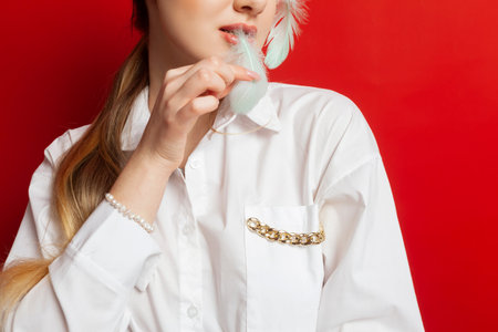 Portrait of a lovely tender girl wearing a feather decorations and posing and holding feathers. Isolated on a red background.の写真素材