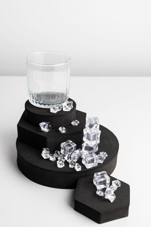 Multilevel black stand with a glass on the very top and scattered ice around. Isolated on white.の写真素材