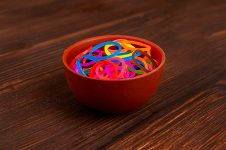 Bowl of a Fancy glowing in darkness rubber bands for hair against a wooden background.