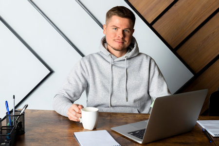 Portrait of a smiling male office worker or IT employee sitting at a desk in modern office with a...