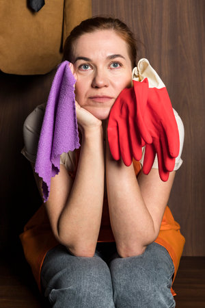 Portrait of a Tired woman from a clening service sitting with a cloth and gloves in the hands and staring off into one point with her gaze.の写真素材