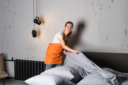 A woman in apron from cleaning service making the bed. Cleaning of furniture.の写真素材