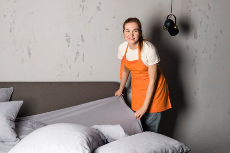 A woman in apron from cleaning service making the bed. Cleaning of furniture.の写真素材