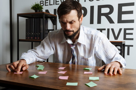 Thoughtful Office worker or employee looking at a bunch of sticky notes, trying to manage all his tasks.の写真素材