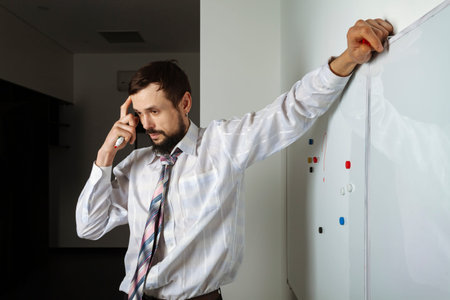 Thoughtful businessman or employee in the office moving colorful magnets on a whiteboard, trying to solve business problems.の写真素材