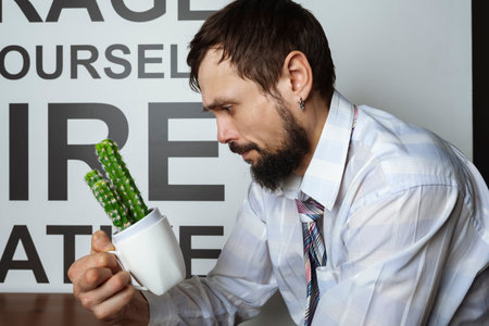 Confused and with a lost gaze, an office worker or businessman looks at a cup with a cactus.
