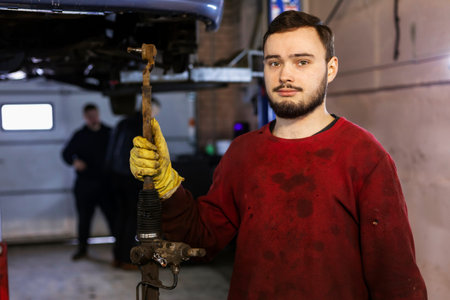 A hardworking mechanic with oil-stained clothing is holding a just-removed old broken steering rack.の写真素材