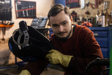 A hardworking mechanic in oil-stained clothing is holding a welding mask.の写真素材