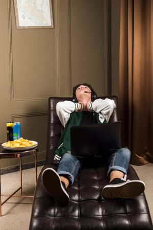 An upset gamer sitting on a couch, leaning back with a laptop after losing. A table next to him with...