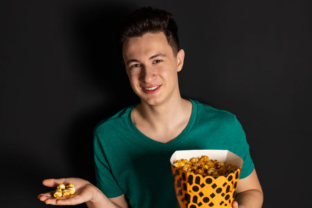 Funny young man sitting on the couch watching movie on notebook pc and eating popcornの写真素材
