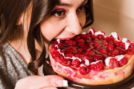 Close up portrait of a hungry young pregnant woman going to eat chocolate cake isolated on a gray backgroundの写真素材
