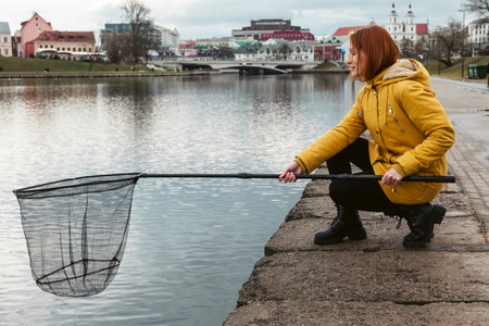 Young redhead girl with fishing net sitting around city lakeの写真素材