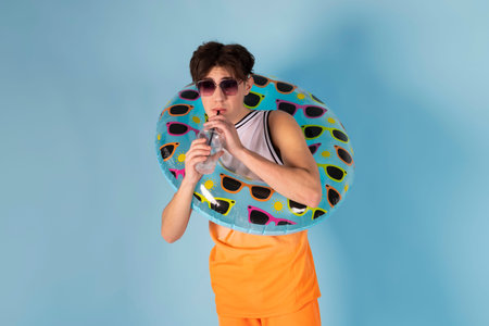 Funny man with blue inflatable swimming circle flaunts his strength on light blue background. Full length of playful strong male swimmer. Summer vacation concept.の写真素材