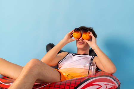 Funny man with blue inflatable swimming circle flaunts his strength on light blue background. Full length of playful strong male swimmer. Summer vacation concept.の写真素材