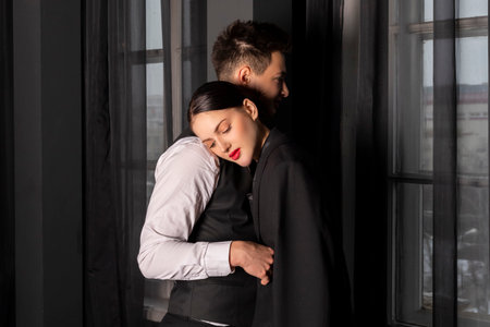 A young elegantly dressed couple in a dark room. The gentleman offers his jacket to the girl so that she does not get cold. Good manners and taking care of a woman.の写真素材