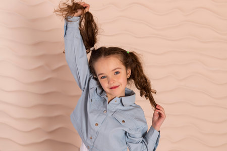 Portrait of a charming little girl, well dressed in a blue shirt with a slight makeup happily pulling her hair or pigtails.の写真素材