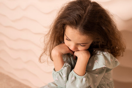 Close-up Portrait of a charming little girl, well dressed in a pastel green dress with a slight makeup and brown loose hair, posing over a beige wavy background.の写真素材