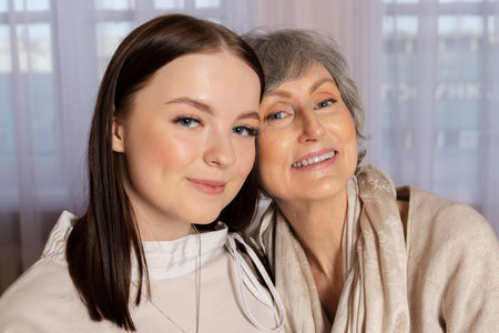 A grandmother or elderly woman and granddaughter or young girl are having a sweet and friendly conversation while sitting on a couch. Strong, loving, and happy family.の写真素材