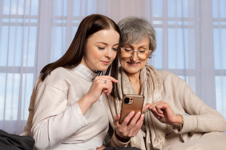 A young girl is explaining to an elderly woman how to use a phone. The granddaughter is showing her phone to her grandmother. a family pastime, helping and respecting the elderly.の写真素材