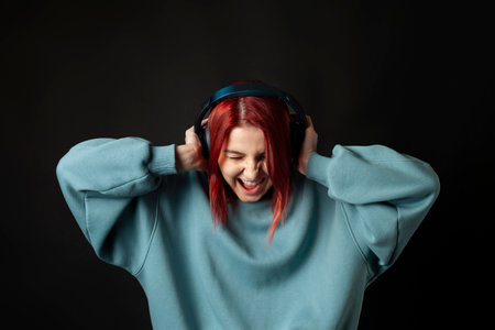Charming young redhead girl in a blue oversized hoodie enjoying the music with a headphones.の写真素材