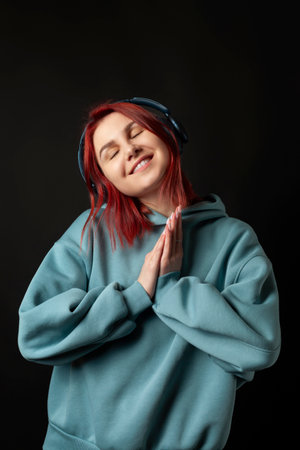 Charming young redhead girl in a blue oversized hoodie enjoying the music with a headphones.の写真素材