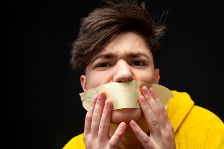 A young guy in a yellow pajama with a taped mouth. freedom of speech issues concept.の写真素材
