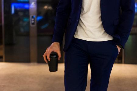 A successful businessman in a dark blue suit with a coffee cup, going through the mall. shop owner.の写真素材