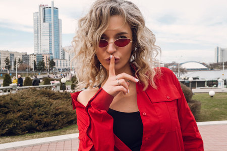 Street photography. A happy stylish girl in red glasses and an unbuttoned shirt looking at the...