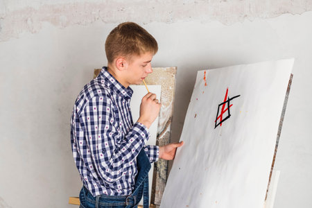 Thoughtful painter or artist In a denim overalls and checkered shirt working on a new art in a...