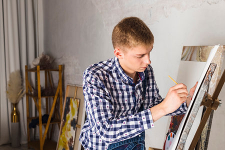 Thoughtful painter or artist In a denim overalls and checkered shirt working on a new art in a workshop.の写真素材