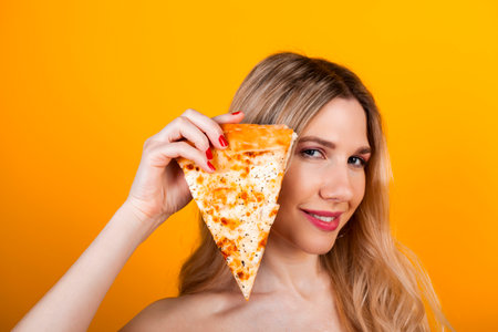 A beautiful fit young blonde girl posing with a pizza slice. Isolated on yellow.の写真素材