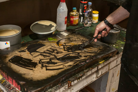 The artist is mixing paint and chemicals with a spatulas in a Lithographic art workshop.