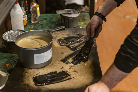 The artist is mixing paint and chemicals with a spatulas in a Lithographic art workshop.