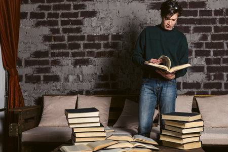 A hard learning student dressed neatly, in round glasses is reading and studying among piles and stacks of books.の写真素材