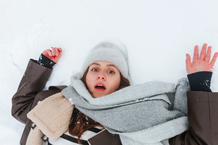 Surprised and shocked brunette girl lying on the snow. Woman slipped and fell on the ground at winter.の写真素材
