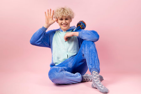 A curly blond guy in a cute and funny blue pajama pretends to be a kid, teasing and gesturing,...