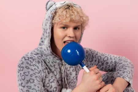 A curly blond guy in a cute and funny gray spotted animal pajamas, pretends to be a kid, holds and...