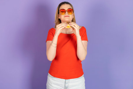 Excited hungry pretty girl eats fast food, cheap burger, holding fries and burger. fast food and...