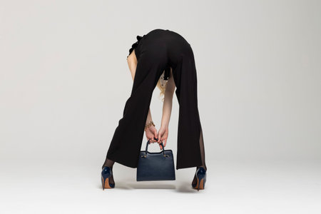 Young Curly blonde girl elegantly dressed,picking up a handbag from the floor, reaching down, rear view. expensive clothes, style and fashion concept.の写真素材