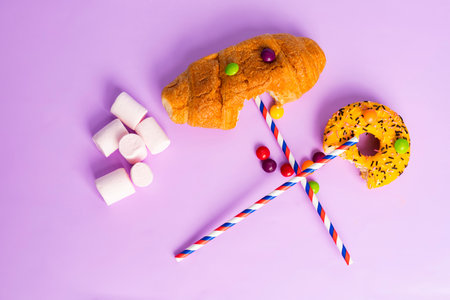 Creatures made of sweets, candies, donuts, marshmallows and colorful straws. isolated on pastel purple background. flat lay. top view.の写真素材