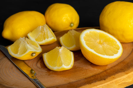 Fresh, bright yellow whole and cut lemons lying on a wooden cutting board. isolated on black, dark gray background.の写真素材