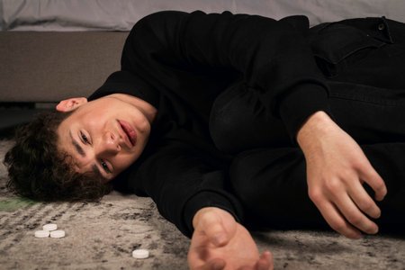 A severely depressed guy, lying on the floor among pills and a bottle of alcohol. A young man in a hard mental condition. alcohol and drugs addiction.の写真素材