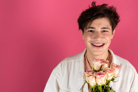 Happy handsome young man in white denim jacket with bouquet of roses going to a date. Isolated on pink.の写真素材