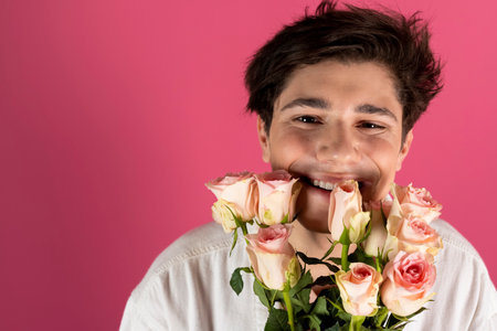 Happy handsome young man in white denim jacket with bouquet of roses going to a date. Isolated on pink.の写真素材