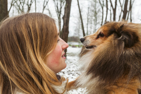 A young blonde girl and her Miniature Sheltie dog, walking in the snowy forest or park, enjoying the nature. Dog walk in a winter day.の写真素材