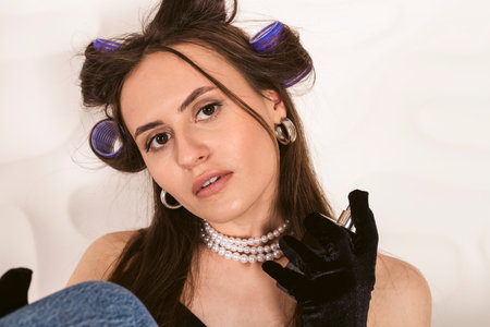 Portrait of A beautiful girl in a corset and elbow length gloves with hair in curlers, putting on perfume, getting ready for an elegant evening meeting or party.の写真素材