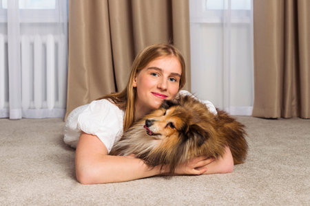 Adorable aged Miniature Sheltie dog and its owner, cute blonde girl are spending time together indoors. Strong friendship and funny leisure with the pet.の写真素材