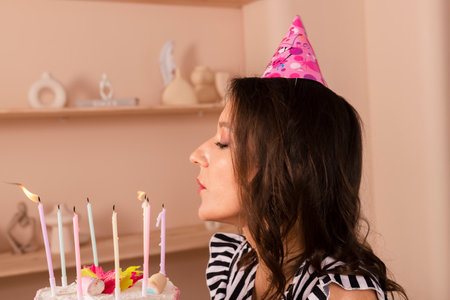 Beautiful brunette woman celebrating her birthday, dressed in a striped short dress and a birthday...